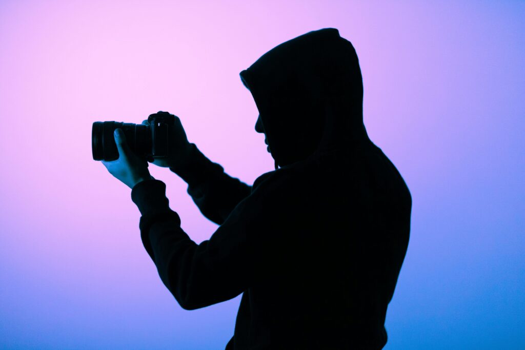 A silhouette of a hooded photographer capturing a shot with a camera in a softly lit studio.